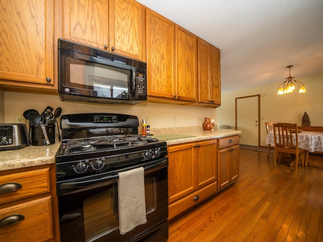 kitchen with an inviting chandelier, dark hardwood / wood-style floors, light stone counters, and black appliances