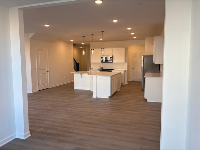 kitchen with appliances with stainless steel finishes, a kitchen island with sink, pendant lighting, dark hardwood / wood-style floors, and white cabinetry