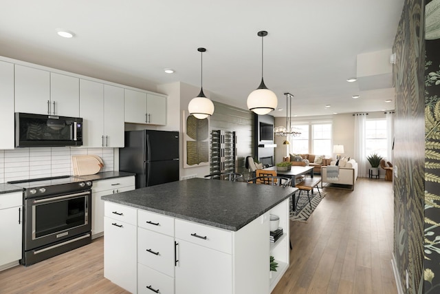 kitchen with black appliances, hanging light fixtures, a kitchen island, light hardwood / wood-style floors, and white cabinetry