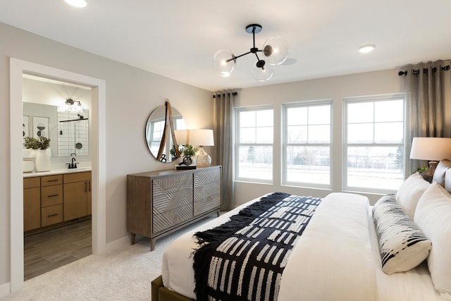 carpeted bedroom featuring a chandelier, ensuite bathroom, and sink