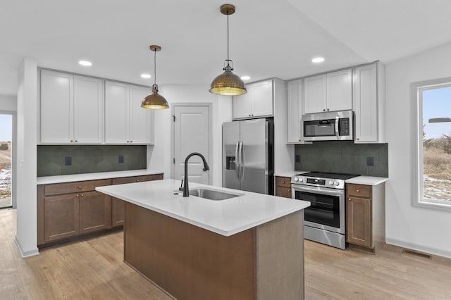 kitchen featuring pendant lighting, a kitchen island with sink, sink, light hardwood / wood-style floors, and stainless steel appliances