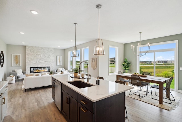 kitchen featuring light stone counters, sink, light hardwood / wood-style flooring, dishwasher, and a fireplace