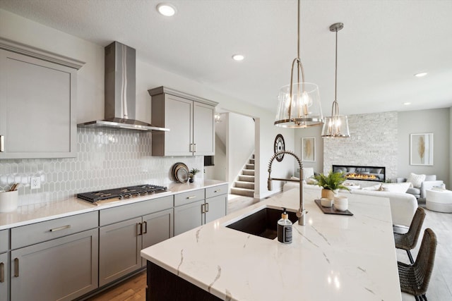 kitchen with stainless steel gas stovetop, wall chimney range hood, sink, hardwood / wood-style flooring, and an island with sink