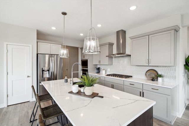 kitchen featuring a large island, wall chimney exhaust hood, light hardwood / wood-style floors, and appliances with stainless steel finishes