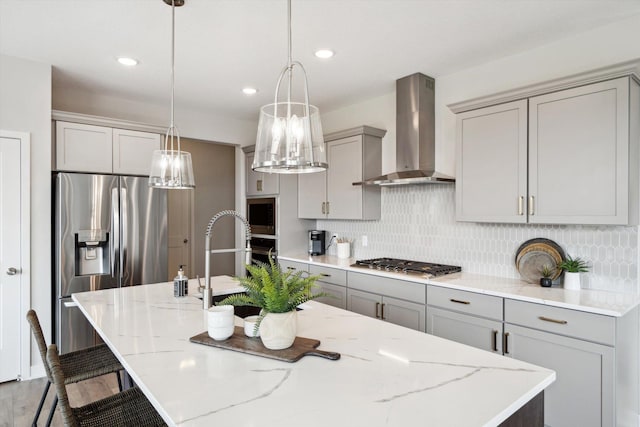 kitchen with hanging light fixtures, wall chimney range hood, an island with sink, and appliances with stainless steel finishes