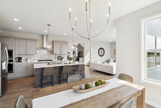 kitchen with pendant lighting, sink, wall chimney exhaust hood, gray cabinets, and dark hardwood / wood-style flooring