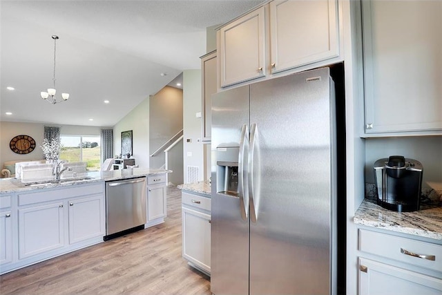 kitchen with appliances with stainless steel finishes, light wood-type flooring, vaulted ceiling, sink, and pendant lighting