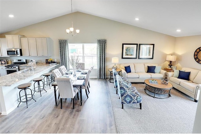 living room featuring light wood-type flooring, high vaulted ceiling, and a chandelier