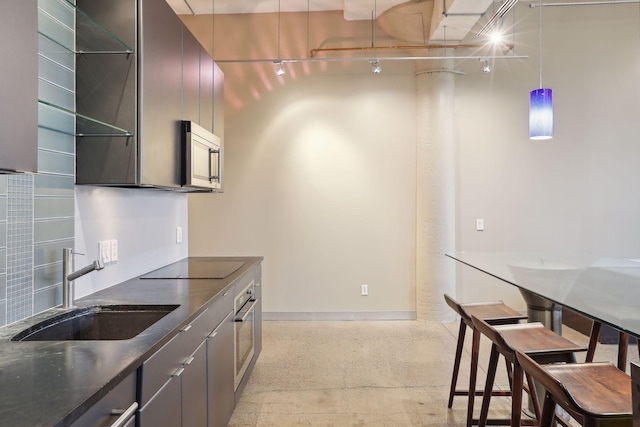 kitchen with dark countertops, modern cabinets, a sink, baseboards, and appliances with stainless steel finishes