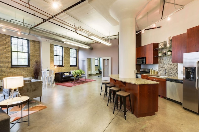 kitchen featuring a high ceiling, a sink, appliances with stainless steel finishes, open floor plan, and a breakfast bar area
