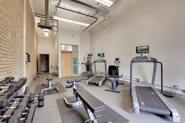 exercise room with brick wall and a towering ceiling