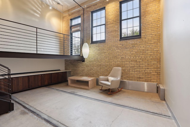 sitting room with concrete floors, a high ceiling, and brick wall