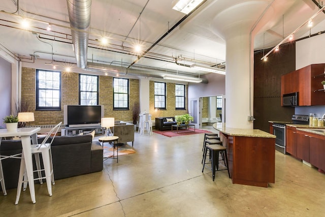 kitchen featuring open floor plan, modern cabinets, brick wall, a kitchen bar, and appliances with stainless steel finishes
