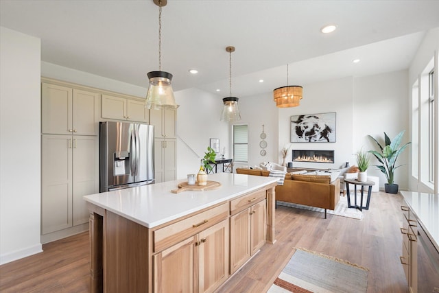 kitchen with a kitchen island, decorative light fixtures, stainless steel appliances, cream cabinets, and light hardwood / wood-style flooring