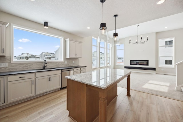 kitchen featuring pendant lighting, sink, dishwasher, a center island, and dark stone counters