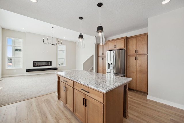 kitchen with hanging light fixtures, a center island, light stone counters, stainless steel refrigerator with ice dispenser, and light wood-type flooring