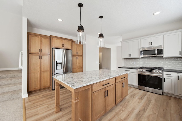 kitchen featuring appliances with stainless steel finishes, hanging light fixtures, light stone counters, white cabinets, and a kitchen island