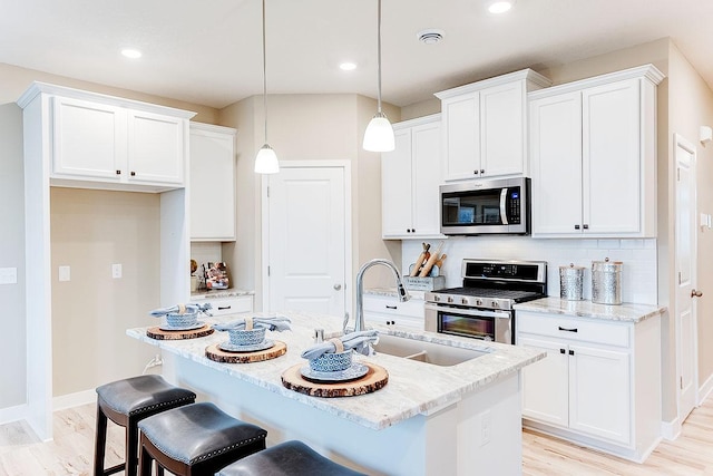 kitchen with a kitchen island with sink, sink, pendant lighting, and appliances with stainless steel finishes