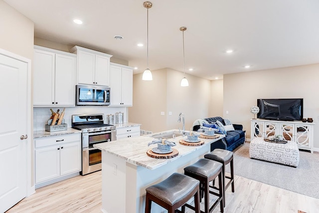 kitchen with light stone countertops, sink, stainless steel appliances, light hardwood / wood-style flooring, and decorative light fixtures