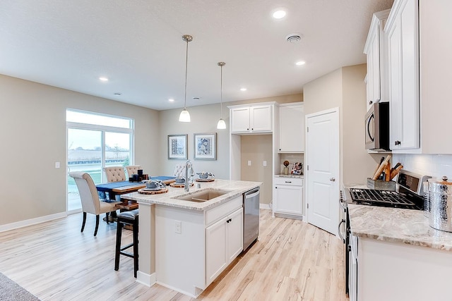 kitchen with white cabinets, sink, an island with sink, appliances with stainless steel finishes, and decorative light fixtures