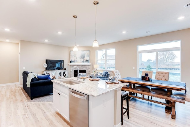 kitchen with hanging light fixtures, stainless steel dishwasher, an island with sink, a wealth of natural light, and white cabinetry