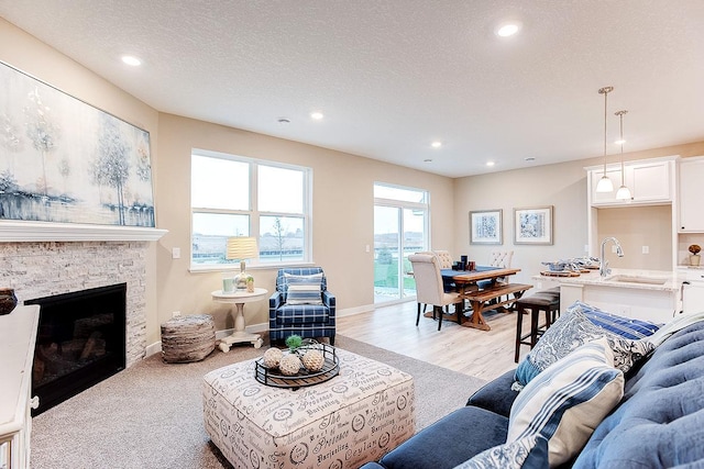 living room featuring a textured ceiling, sink, light wood-type flooring, and a fireplace