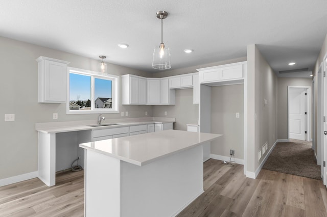 kitchen with sink, white cabinets, hanging light fixtures, a center island, and light wood-type flooring