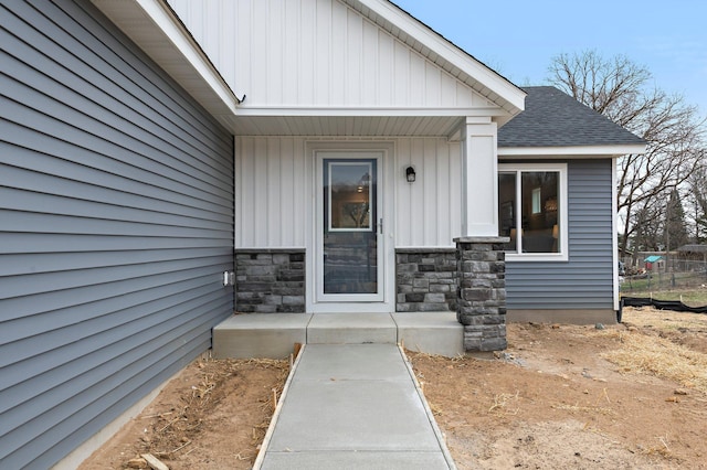 doorway to property featuring board and batten siding, roof with shingles, and stone siding