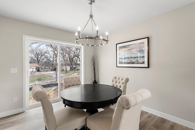 dining area with light wood-type flooring, baseboards, and an inviting chandelier