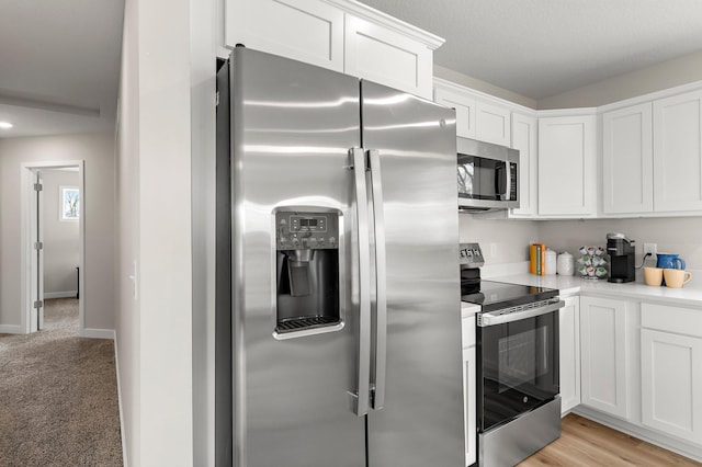 kitchen with white cabinets, light countertops, light carpet, baseboards, and appliances with stainless steel finishes