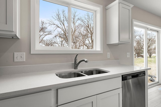 kitchen with light countertops, dishwasher, white cabinetry, and a sink