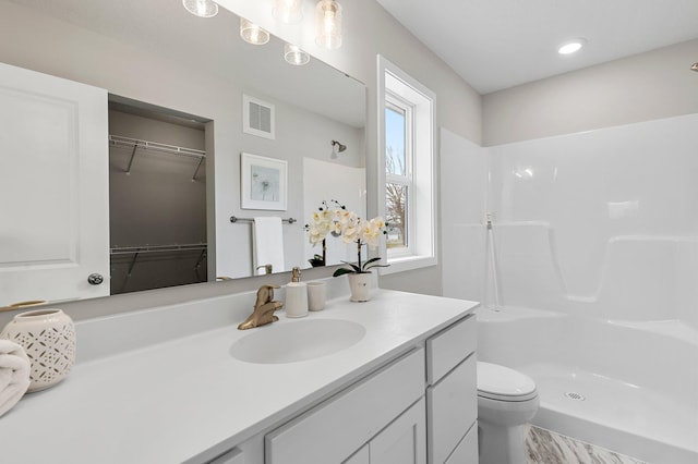bathroom featuring a walk in closet, vanity, walk in shower, toilet, and visible vents