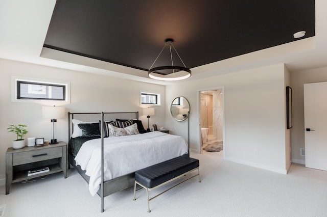 bedroom with light carpet, a tray ceiling, and ensuite bathroom