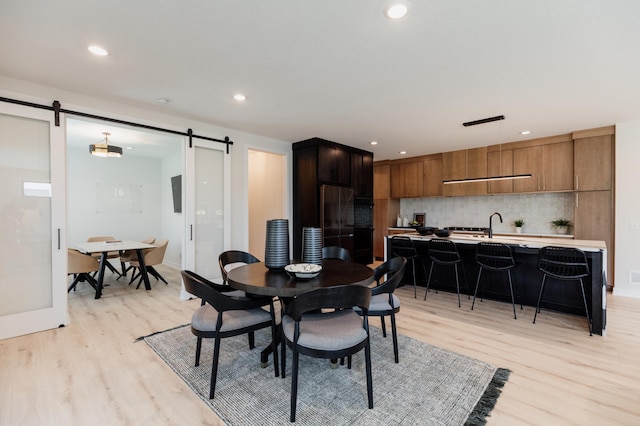 dining space with a barn door, light hardwood / wood-style flooring, and sink