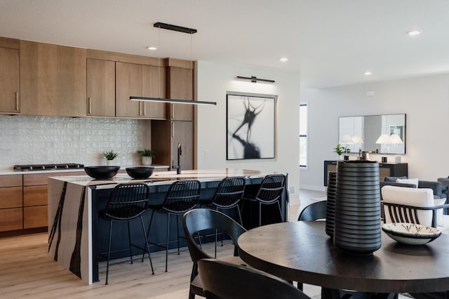 kitchen featuring tasteful backsplash, light hardwood / wood-style flooring, an island with sink, and hanging light fixtures