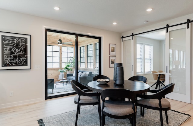 dining space with a barn door, ceiling fan, and light wood-type flooring