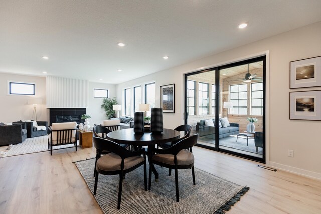 dining room featuring a tile fireplace, a wealth of natural light, and light wood-type flooring