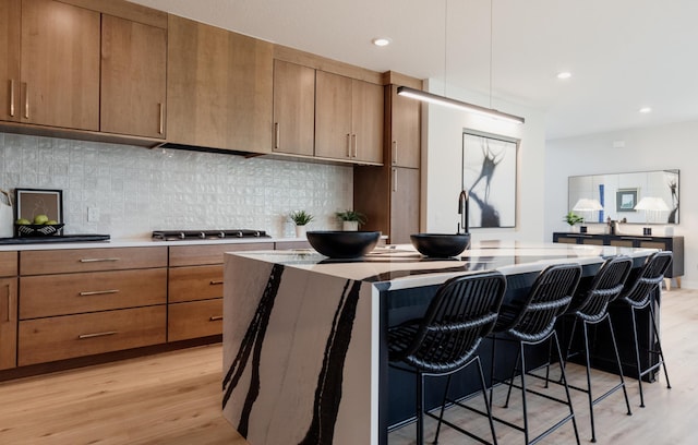 kitchen with light hardwood / wood-style floors, a kitchen island, a breakfast bar area, and stainless steel gas cooktop