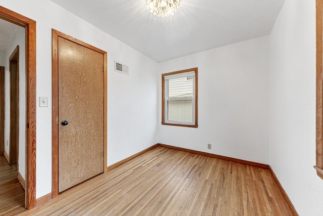 unfurnished room featuring a chandelier and light wood-type flooring