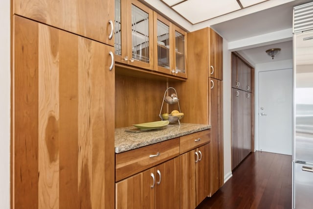 bar featuring built in refrigerator, light stone counters, and dark hardwood / wood-style floors