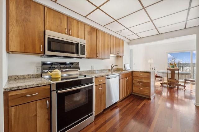 kitchen with light stone countertops, sink, stainless steel appliances, dark wood-type flooring, and a paneled ceiling