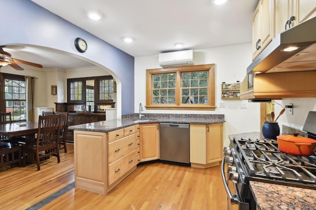 kitchen with sink, appliances with stainless steel finishes, a wall mounted AC, light brown cabinetry, and dark stone counters