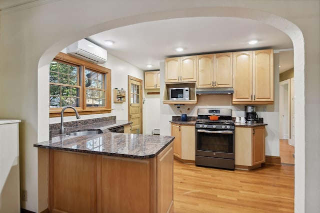 kitchen with sink, light brown cabinets, an AC wall unit, appliances with stainless steel finishes, and dark stone counters