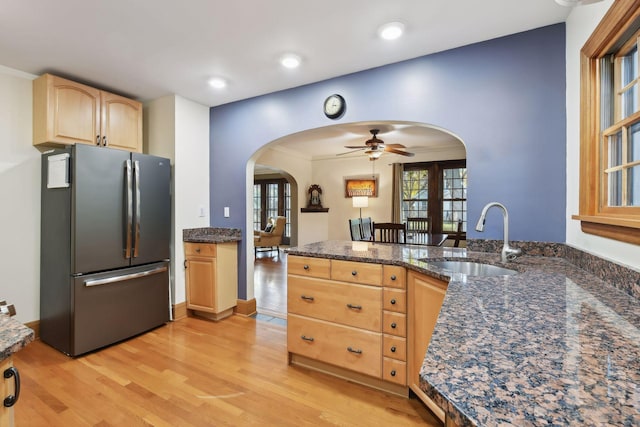 kitchen with sink, stainless steel fridge, dark stone counters, light brown cabinets, and light wood-type flooring