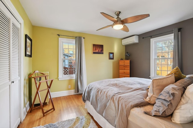 bedroom with a closet, an AC wall unit, ceiling fan, and light hardwood / wood-style flooring