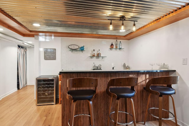 bar featuring wooden ceiling, a tray ceiling, beverage cooler, and light wood-type flooring