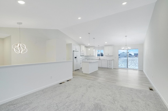 unfurnished living room with sink, light carpet, vaulted ceiling, and a notable chandelier