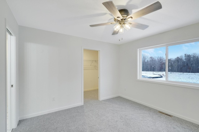 unfurnished bedroom with a closet, light colored carpet, a water view, ceiling fan, and a spacious closet