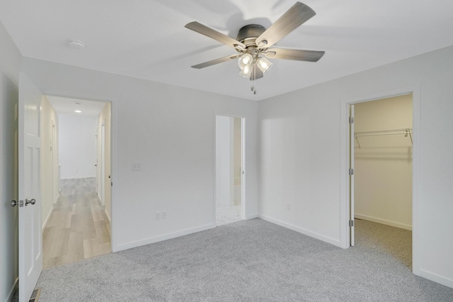 unfurnished bedroom with ceiling fan, a closet, a spacious closet, and light carpet