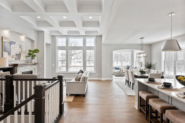 living room featuring a fireplace, beamed ceiling, a chandelier, coffered ceiling, and dark wood-type flooring